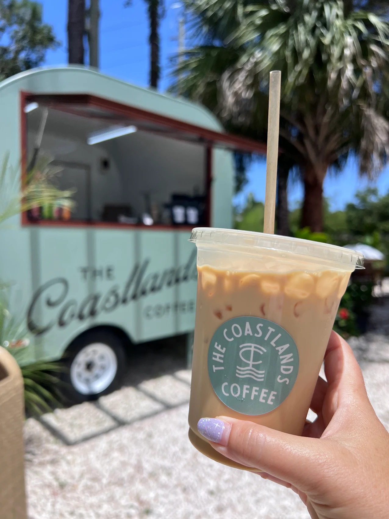 A customer holding a branded iced latte in front of the Coastlands coffee trailer.