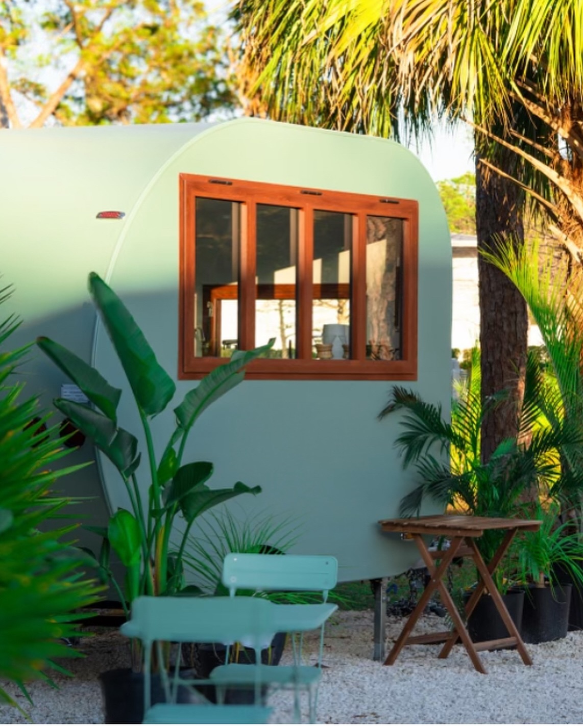 The green Coastlands trailer surrounded by palms and outdoor seating.