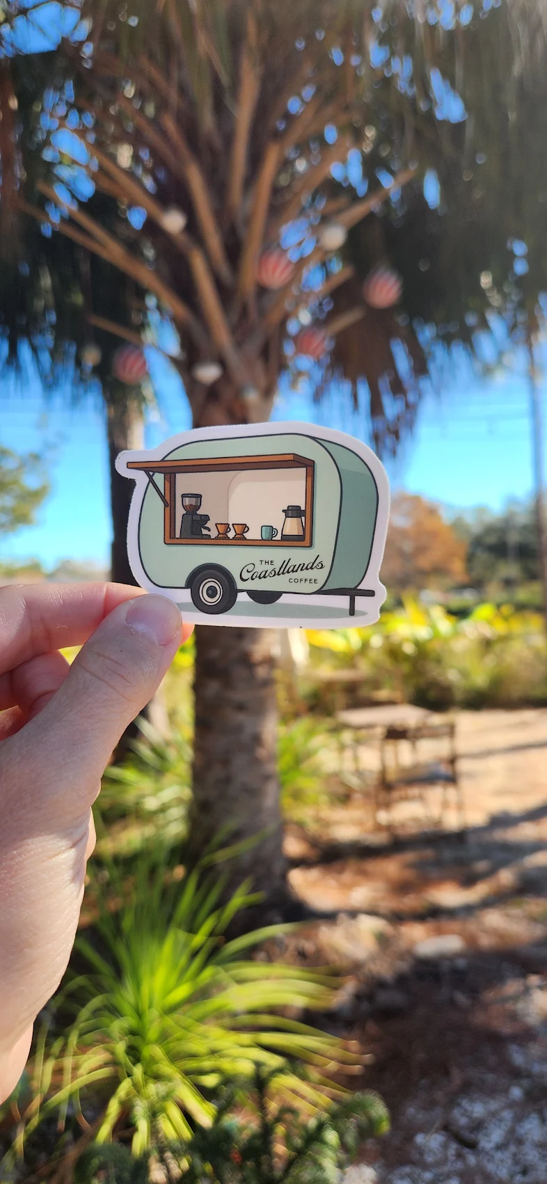 A customer holding a Coastlands trailer sticker in the palm-filled courtyard.